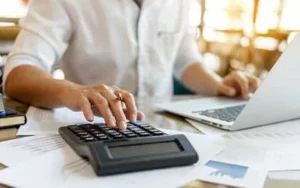 A person uses a calculator and typing on a laptop